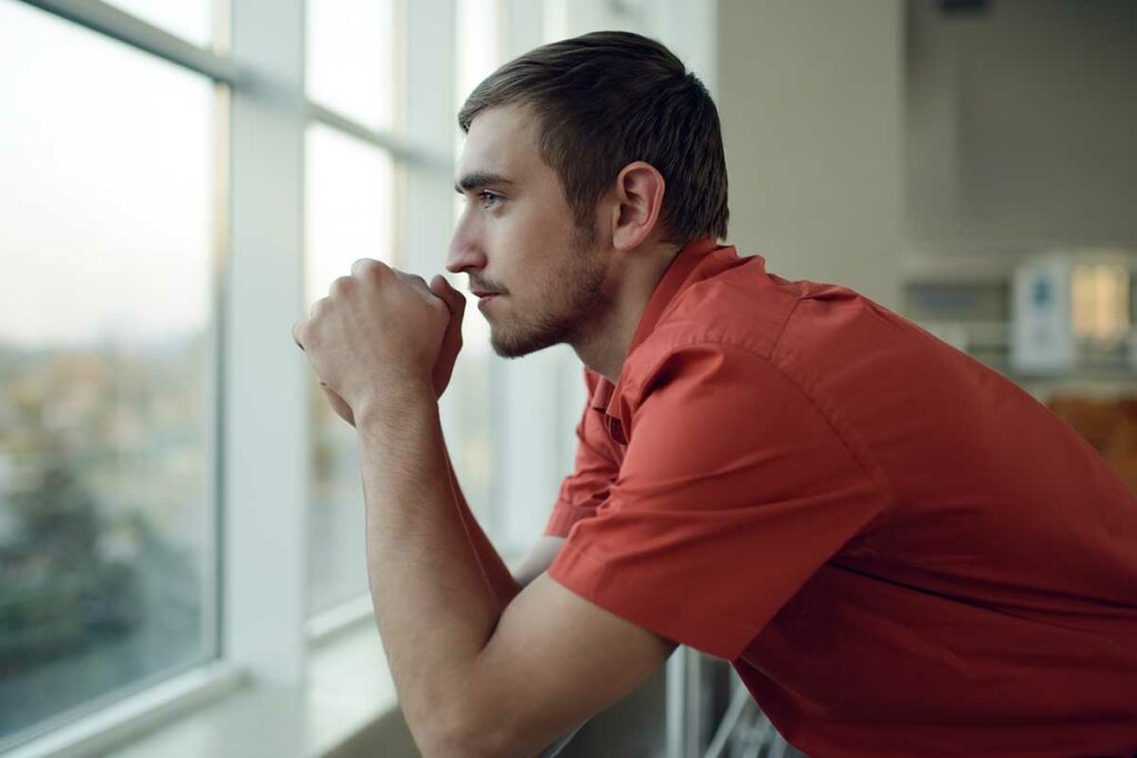 man looks out of window and considers the warning signs of alcohol abuse