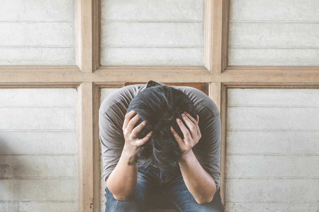 a person puts their head in their hands while experiencing challenging symptoms of bipolar disorder