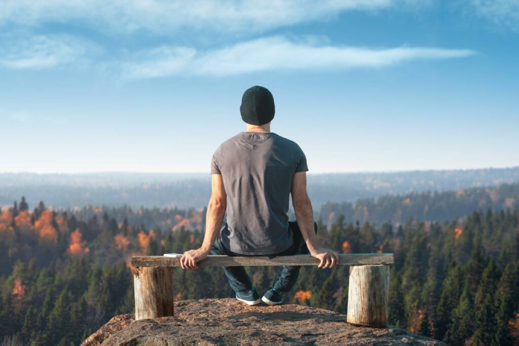 a person sits on a bench looking over a valley to show ways to cope with anxiety