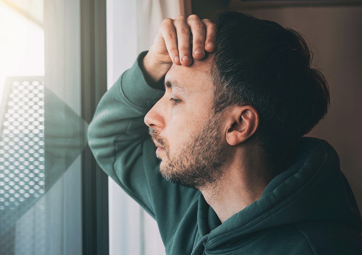 a person looks exhausted as they look out a window wondering about the causes of bipolar disorder