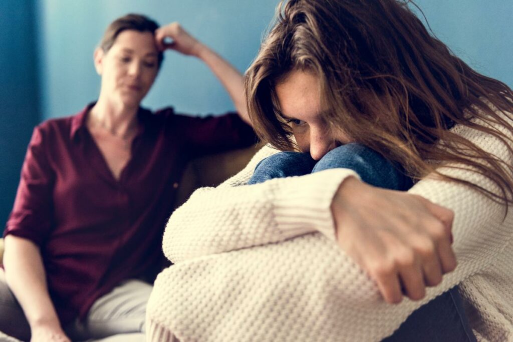 a teen rests their head in their arms while a parent looks upset to show how to help a teenager who doesn't want help