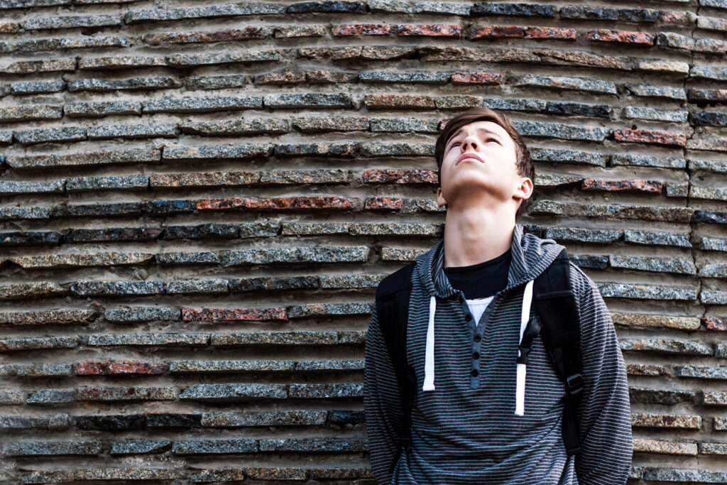 a teen looks up against a brick wall while experiencing causes of depression in teens