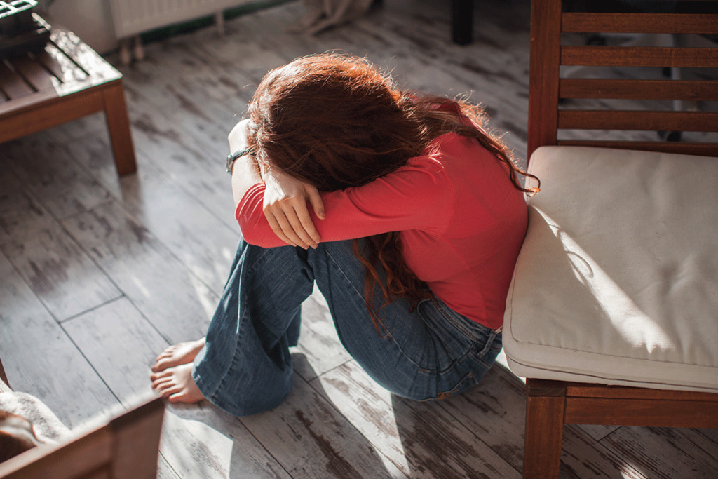 a person sits on the floor with their head in their arms after a self harm relapse