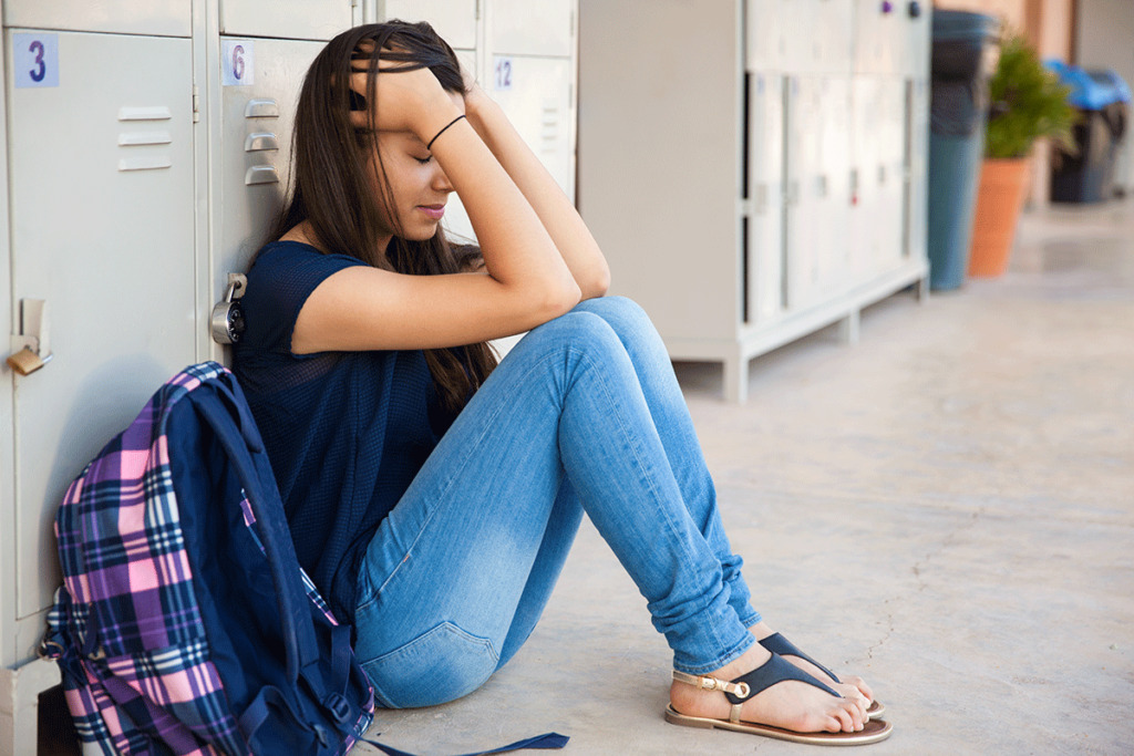 girl sitting on concrete wonders about the causes of anxiety in teens