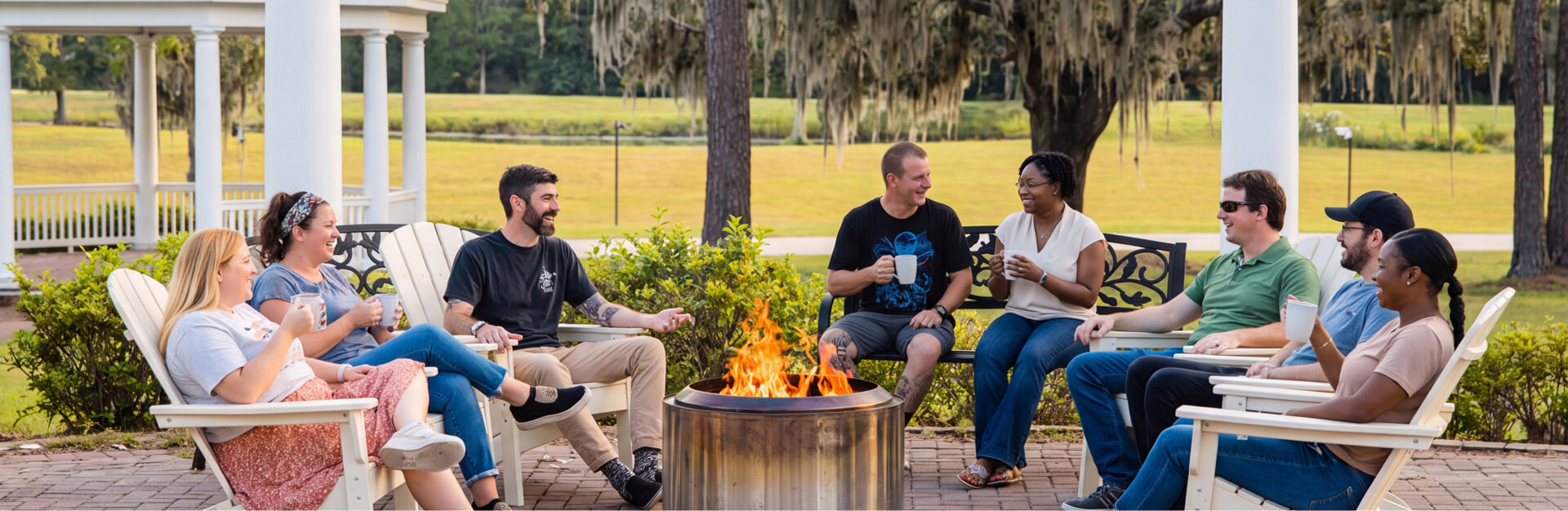 A group of adults sitting around fire talking to each other in a cheerful mood