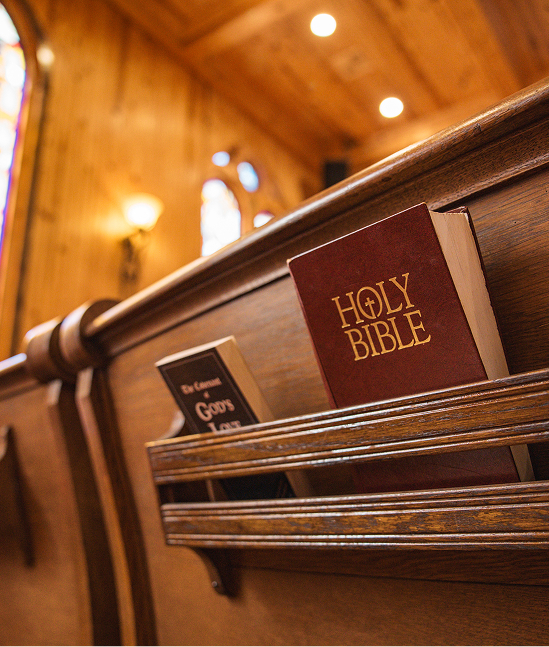 The Holy Bible and two other books at the back of a church pew